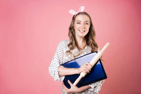 young woman cook or pastry chef runs a business and takes orders in an online store, a cook in an apron holding a laptop in her hands. pastry chef in an apron on a pink background.の写真素材