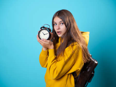Hurry up, concept. A young brunette in a youth hoodie holds an alarm clock in her hands and hurriesの写真素材