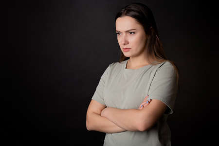 Suspicions, a look from the left. A young brunette woman in a T-shirt, experiencing distrust and doubt, portrait on blackの写真素材