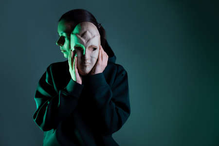 Hiding behind a mask, a young woman in a dark hoodie hides her face with a mask, privacy on the Internet, the concept of information securityの写真素材