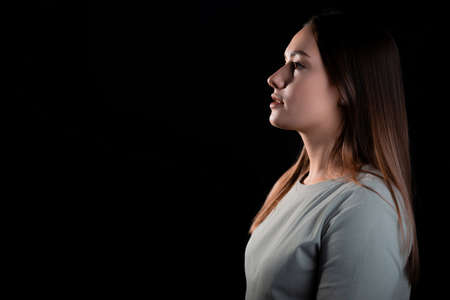 A calm portrait of a young brunette in profile, looking forward. Contour light, copy the space on the left, photo on a black backgroundの写真素材