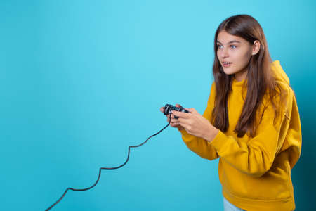 A young woman in a yellow hoodie clutches a gamepad in her hands and looks at the monitor, a gamer in the process of playing on the console , an exciting gameplayの写真素材