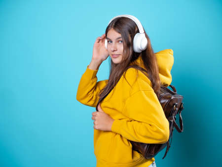 A young smiling student with a backpack and headphones, listening to music or recording a lecture. A young brunette in a bright yellow hoodie uses wireless headphonesの写真素材