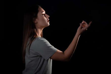 A calm portrait of a young brunette in profile, her gaze and hand are directed forward. Contour light, copy the space on the right, photo on a black backgroundの写真素材