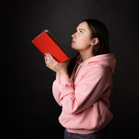Study fatigue, a young student experiences fatigue while reading a textbook. A young brunette in a pink hoodie wearily buried her forehead in a textbook.の写真素材