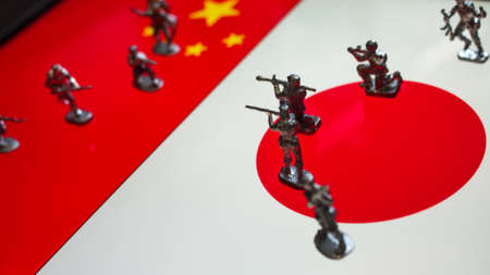 The concept of the economic and political crisis between Japan and China, toy soldiers attacking each other against the background of national flags.の写真素材