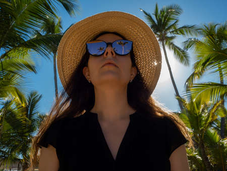 Portrait of a traveler in a straw hat on the beach. A tropical island in the Caribbean. Reflection of palm trees in sunglasses, the mood of vacation and relaxation by the seaの写真素材