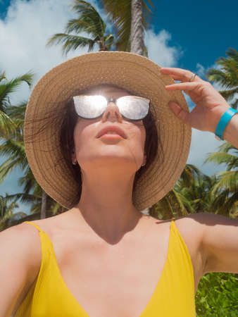 A young woman in sunglasses and a straw hat on a tropical island. Reflection of the sky in...
