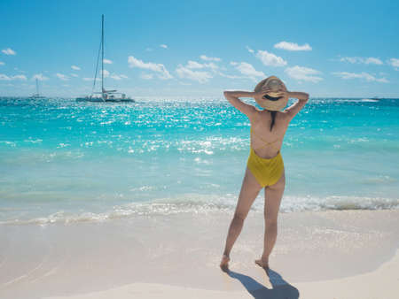 A young woman in a yellow swimsuit on the beach, enjoying a vacation by the sea. Beautiful landscape, white sand and blue waterの写真素材