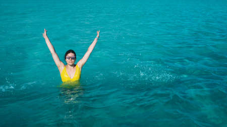 A young woman in a yellow swimsuit is bathing in the azure sea, beautiful clear water. Vacation on a tropical islandの写真素材