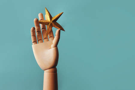 A star in your hand, striving for a dream. A golden star in a wooden hand, the concept of an ambitious dreamer, blue backgroundの写真素材