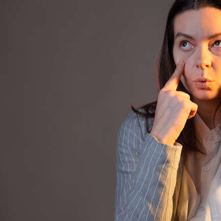 Lack of sleep and chronic fatigue syndrome in workers. A young woman in a jacket forcibly opens her eyes to be productive at work. Portrait on a gray backgroundの写真素材