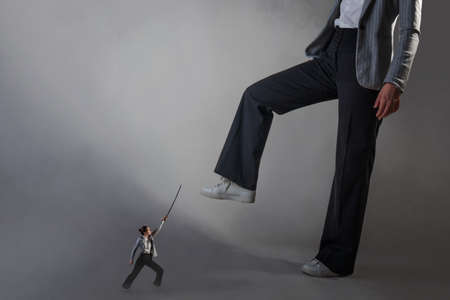 Battle with your fears, professional sphere. A young woman in a business suit with a saber in her hands is fighting with a giant.の写真素材