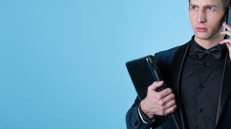 A successful and positive young man in a business suit with a laptop in his hands, talking on the phone, photo on blueの写真素材