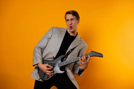 rock  n  roll guy, a cool guy with a fake guitar, pretends to play music. Fun and emotion. A guy in a jacket with a gaming guitar, playing guitar in a simulatorの写真素材