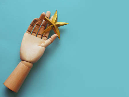 A star in your hand, striving for a dream. A golden star in a wooden hand, the concept of an ambitious dreamer, blue backgroundの写真素材