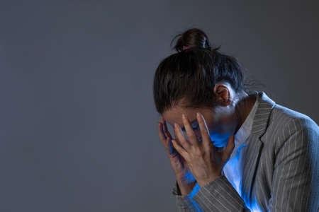 Stress at work and professional burnout. young woman in a business suit standing clutching head, portrait on a gray backgroundの写真素材
