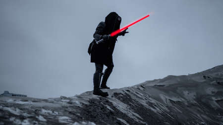 A fantastic assassin in a black suit with a red laser sword against a gray gloomy landscape of a snowy wasteland. dark photo with noise effectの写真素材