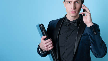 A successful and positive young man in a business suit with a laptop in his hands, talking on the phone, photo on blueの写真素材
