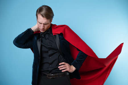 The superhero feels tired and insecure. Impostor syndrome in professionals, concept. A man in a business suit and a red cape.の写真素材