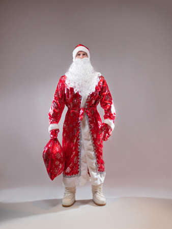 Santa Claus is a traditional Russian grandfather in a red caftan with a bag of gifts. A man in a New Years costume. Childrens holiday, New Years gifts for everyoneの写真素材