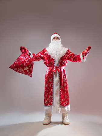 Santa Claus is a traditional Russian grandfather in a red caftan with a bag of gifts. A man in a New Years costume. Childrens holiday, New Years gifts for everyoneの写真素材