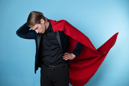 Impostor syndrome in professionals, concept. superhero feels tired and insecure. A man in a business suit and a red cape.の写真素材