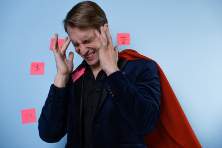 Even superheroes experience professional burnout. A man in the image of a hero in a business suit and a red cape. Tired of the continuous flow of tasks.の写真素材