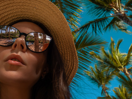 young woman in sunglasses and a straw hat on a tropical island. Reflection of palm trees in sunglasses, the mood of vacation and relaxation by the seaの写真素材