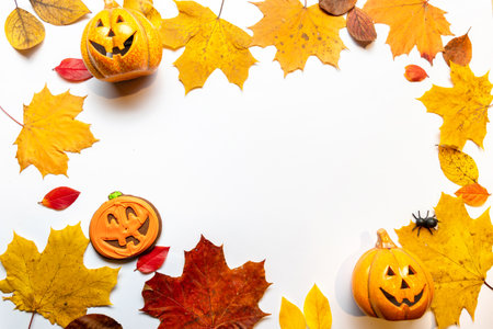 Funny Halloween-themed layout, yellow leaves and pumpkins with a face, top view. White background, copy the space in the centerの写真素材