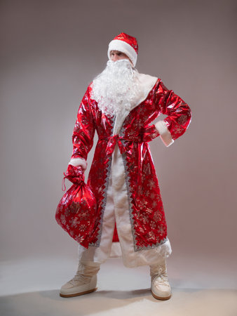 Santa Claus is a traditional Russian grandfather in a red caftan with a bag of gifts. A man in a New Years costume. Childrens holiday, New Years gifts for everyoneの写真素材