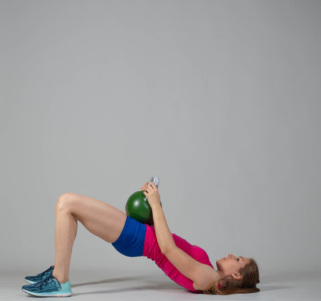 Training with kettlebells, a young athlete performs exercises with kettlebells, pushing the kettlebell up from the lying positionの写真素材