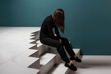Chronic fatigue syndrome, concept. A young woman is sitting wearily on the stairs, a failure when moving up the career ladder, professional burnout.の写真素材