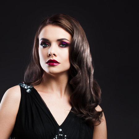 Portrait of a young luxurious woman in a low key. Bright makeup with scarlet lipstick, hairstyle with curls, portrait on a black backgroundの写真素材