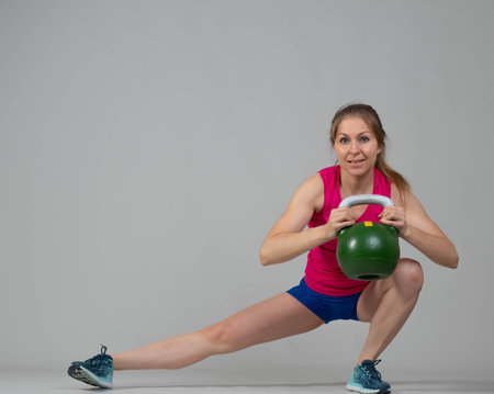 Training with kettlebells, a young athlete performs exercises with kettlebells, lunges with weightsの写真素材