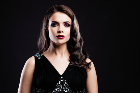 Portrait of a young luxurious woman in a low key. Bright makeup with scarlet lipstick, hairstyle with curls, portrait on a black backgroundの写真素材