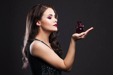 Attractive young brunette woman and a bottle with a new fragrance, use perfume. Portrait on a black backgroundの写真素材