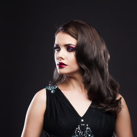 Portrait of a young luxurious woman in a low key. Bright makeup with scarlet lipstick, hairstyle with curls, portrait on a black backgroundの写真素材
