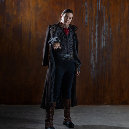Fantasy steampunk action heroine in a long coat. A woman in a retro fantasy outfit on the background of a textured rusty wallの写真素材