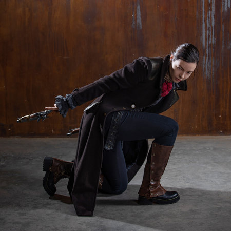 A noble robber with a revolver in a squat, preparing to attack. A woman in a retro fantasy outfit on the background of a textured rusty wallの写真素材