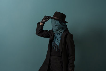 Nobody, the concept of the identity crisis. An impersonal person. The character is wearing a coat and hat, a scarf is wound all over the face. Turquoise backgroundの写真素材