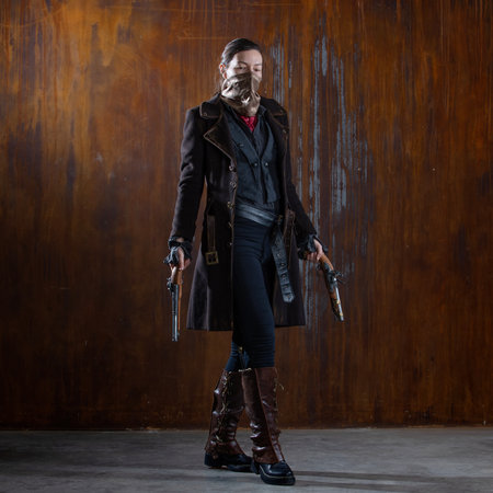 Fantasy steampunk action heroine in a coat with revolvers in her hands. A woman in a retro fantasy outfit on the background of a textured rusty wallの写真素材