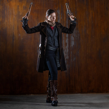 Fantasy steampunk action heroine in a coat with revolvers in her hands. A woman in a retro fantasy outfit on the background of a textured rusty wallの写真素材