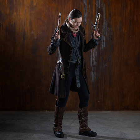 Fantasy steampunk action heroine in a coat with revolvers in her hands. A woman in a retro fantasy outfit on the background of a textured rusty wallの写真素材