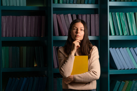 A young woman in the library with a book in her hands, studying and a love of reading. Portrait on the background of bookshelvesの写真素材