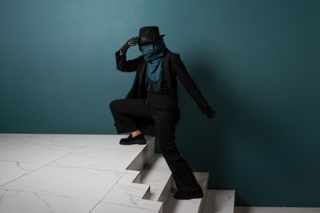 An unknown person, a criminal or a person hiding from the law. Hiding from observation, hiding. A character in a coat and hat with a scarf on his face, sneaks up the stairsの写真素材