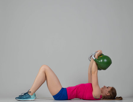 Training with kettlebells, a young athlete performs exercises with kettlebells, pushing the kettlebell up from the lying positionの写真素材
