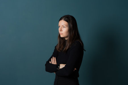 Portrait of a young confident woman, calmly standing against a turquoise wall and looking awayの写真素材