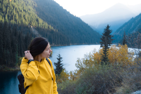 A young female tourist in a yellow hoodie on the background of nature, picturesque mountain lake in the backgroundの写真素材