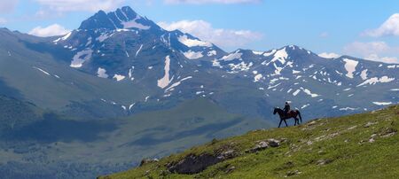 Mountain landscape and shepherd on horse. In the background - mount Magisho. Caucasus mountains. Karachay-Cherkessia. Russia.の写真素材